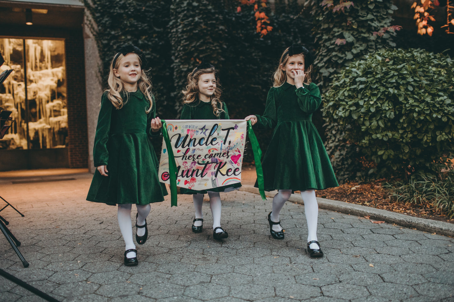 Girls walking into a wedding in a green velvet dresses in a garden.